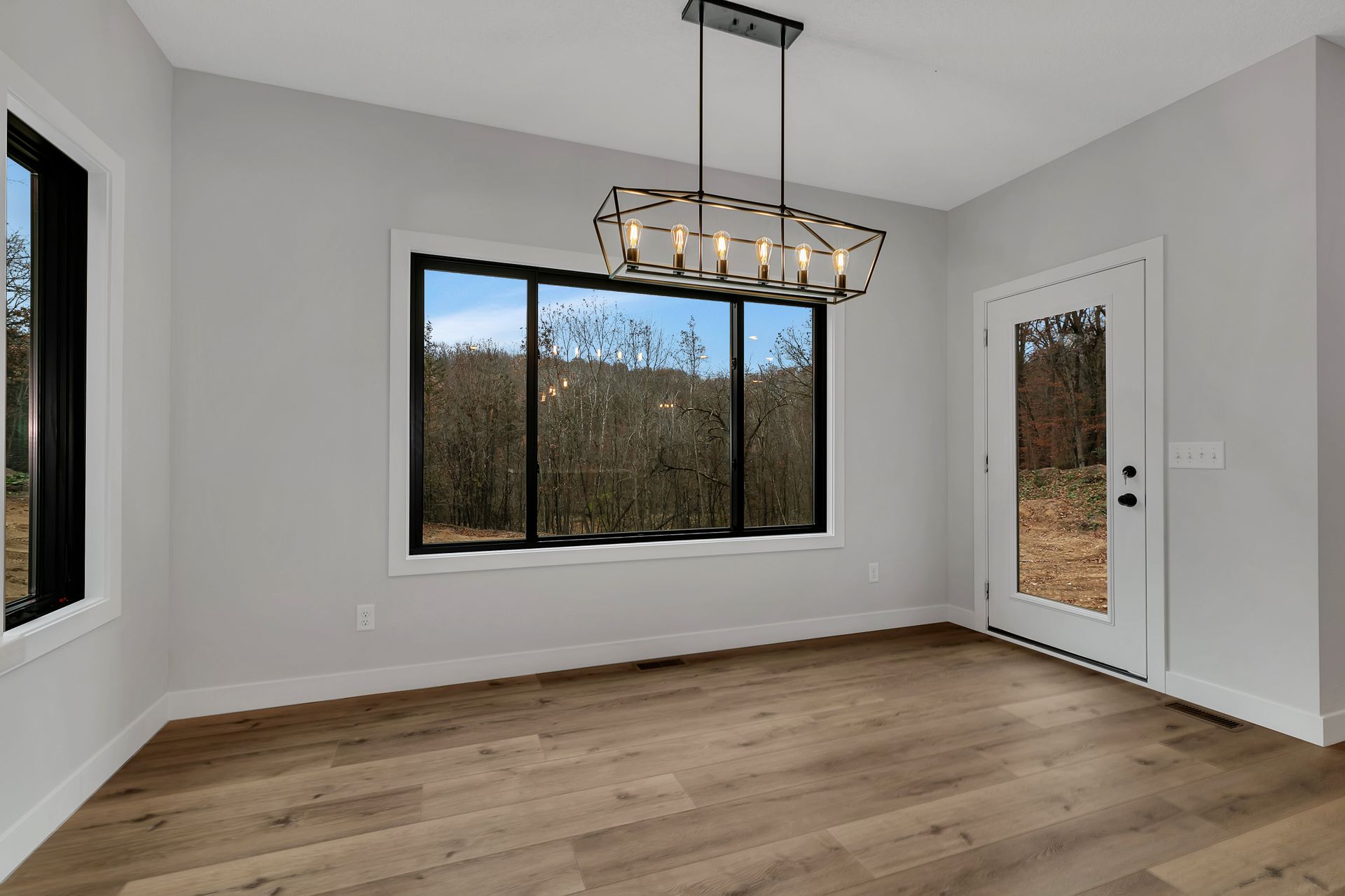 An empty dining room with hardwood floors and a large window.