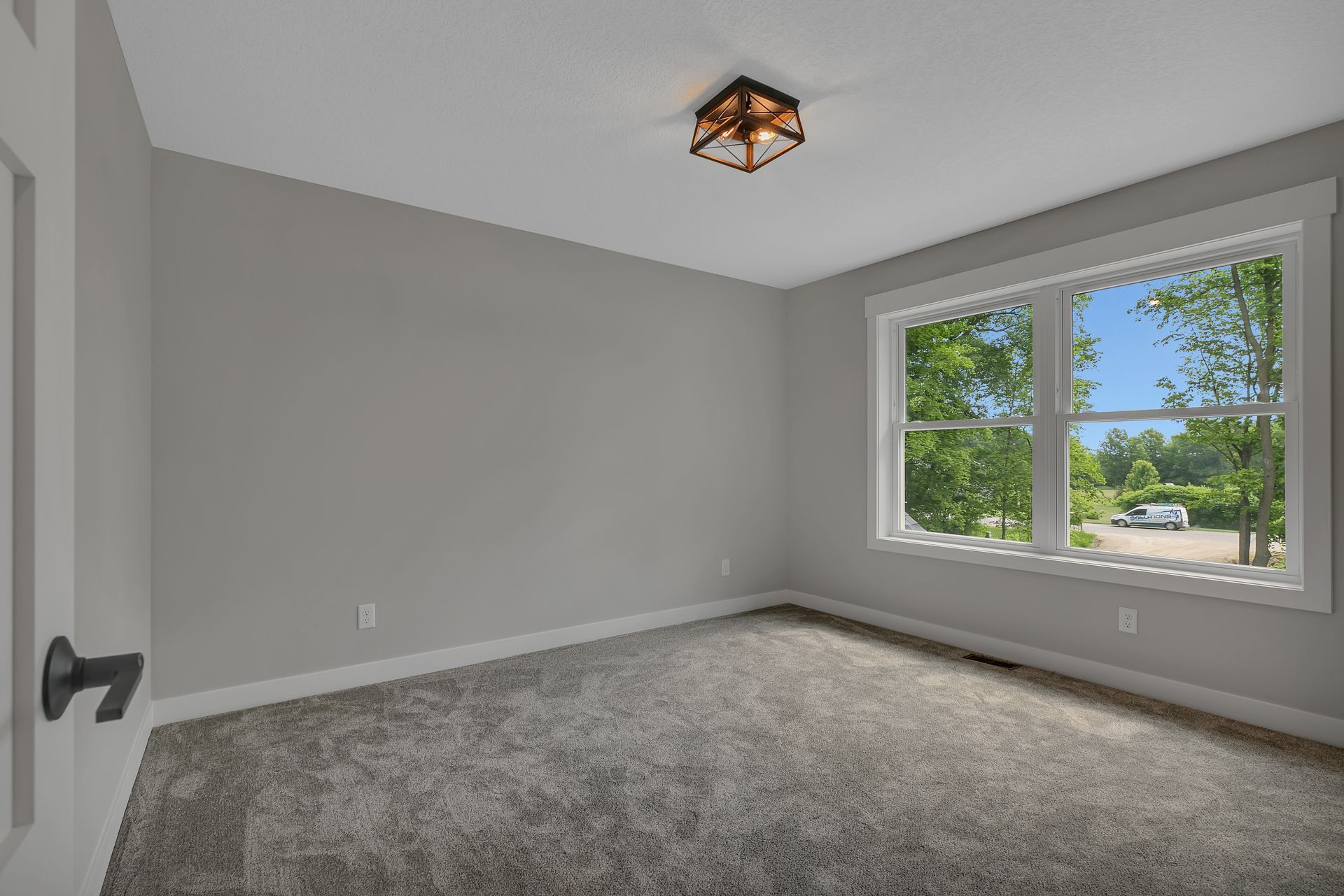 An empty bedroom with a carpeted floor and two windows.