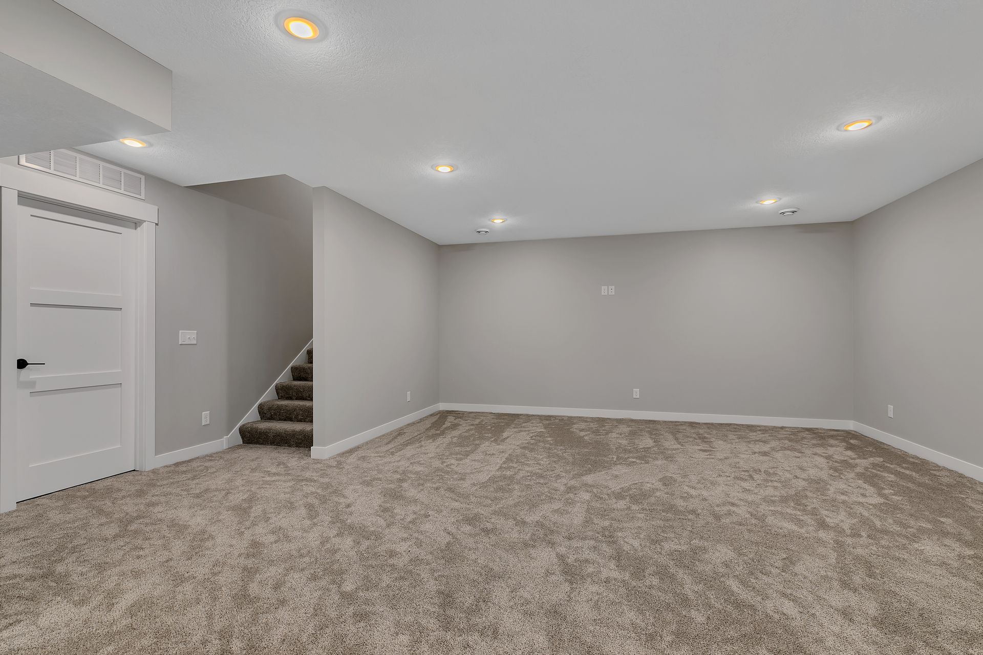 An empty basement with carpeted floors and stairs.