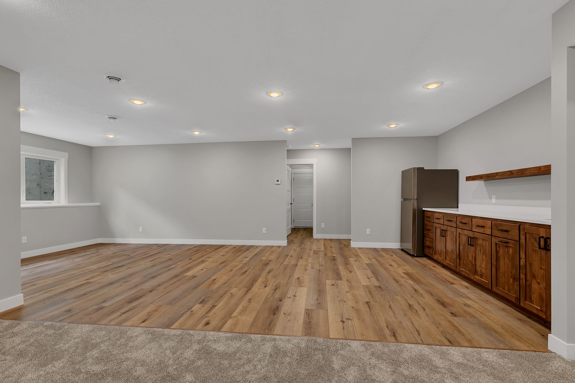 An empty basement with hardwood floors and a refrigerator.