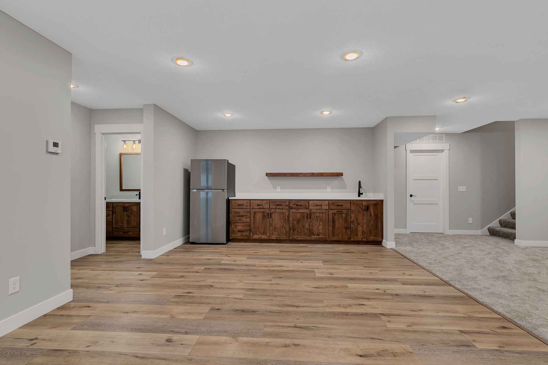 An empty basement with hardwood floors and a refrigerator.