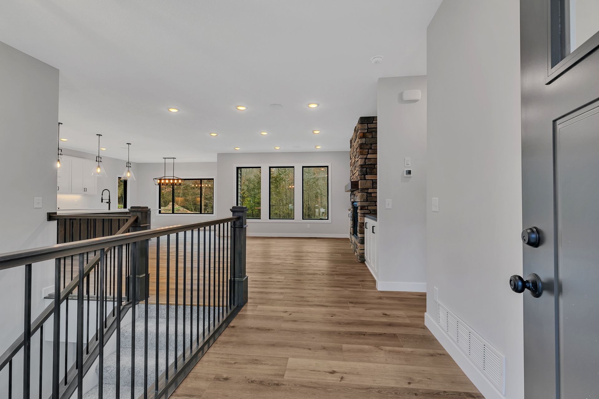 A hallway in a house with hardwood floors and a black railing.