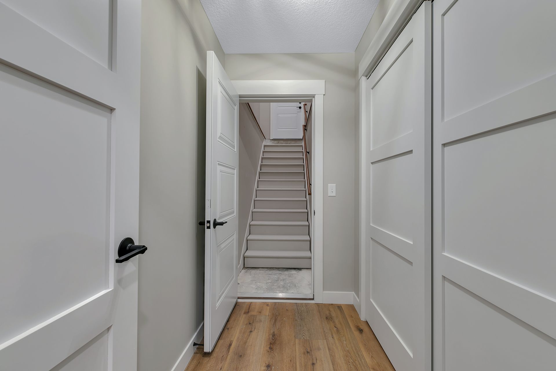 A hallway with hardwood floors and white doors leading to a staircase.