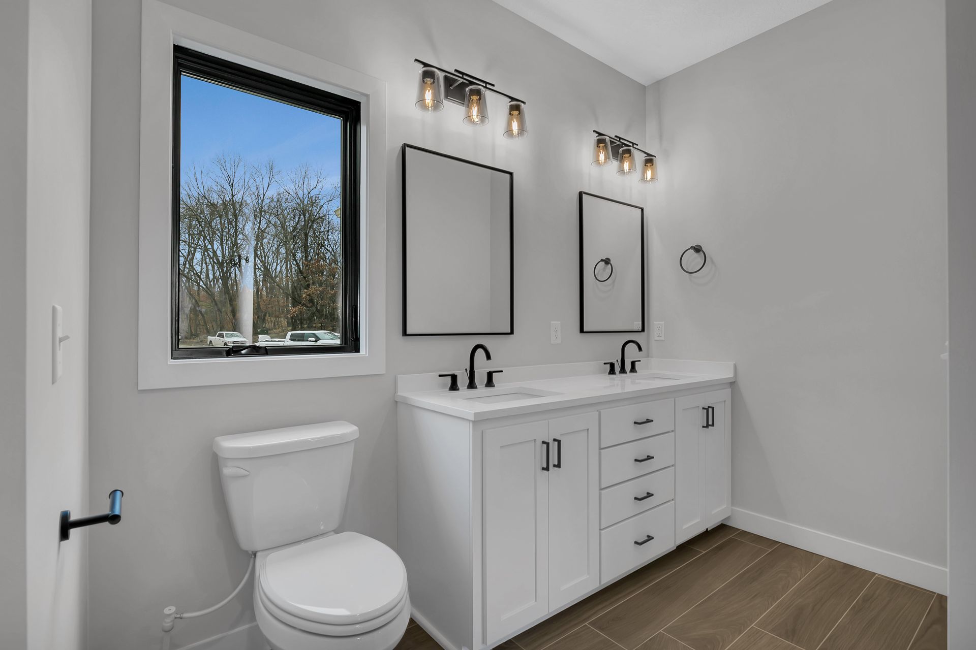 A bathroom with a toilet , sink , mirror and window.