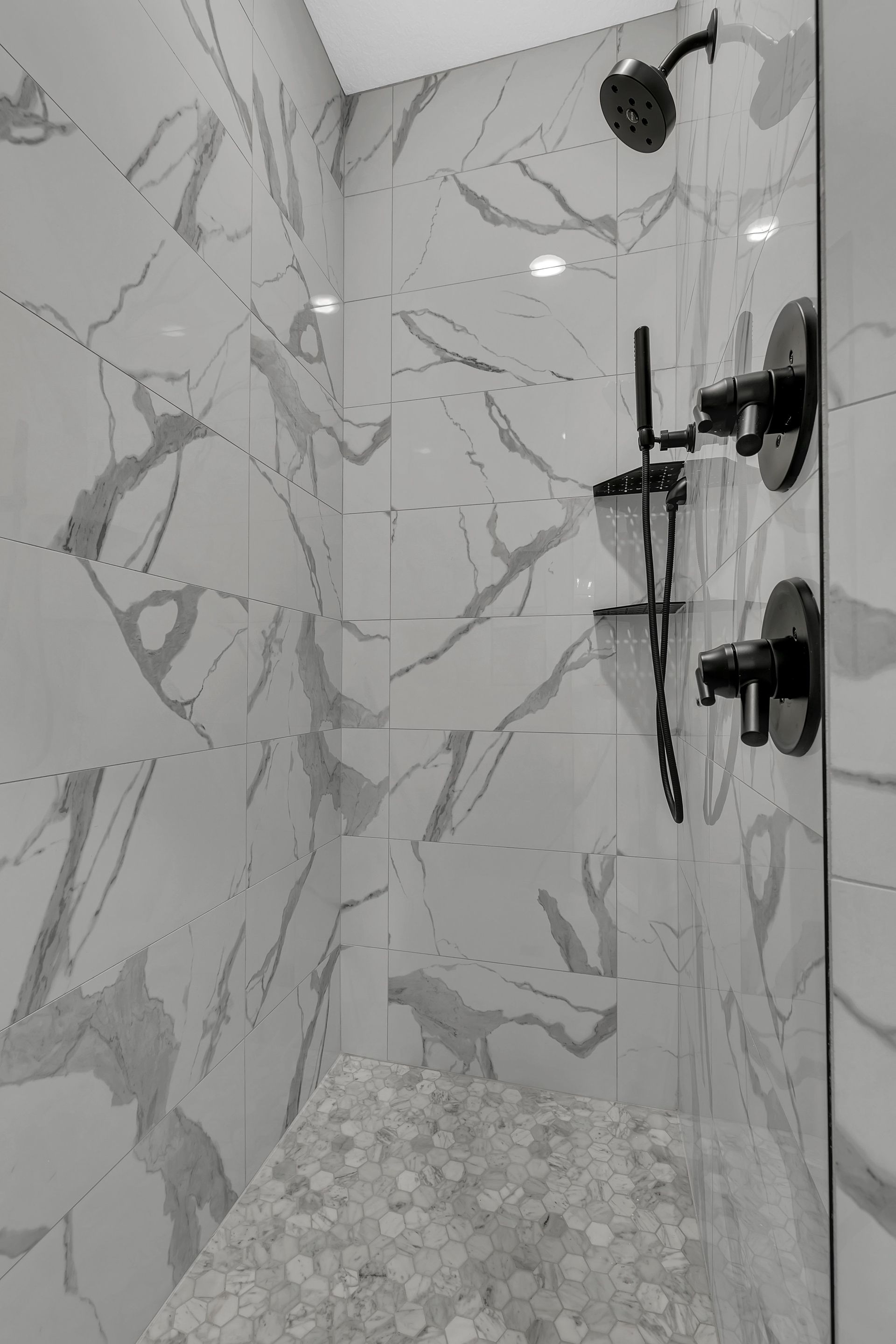A black and white photo of a shower with marble tiles and a shower head.