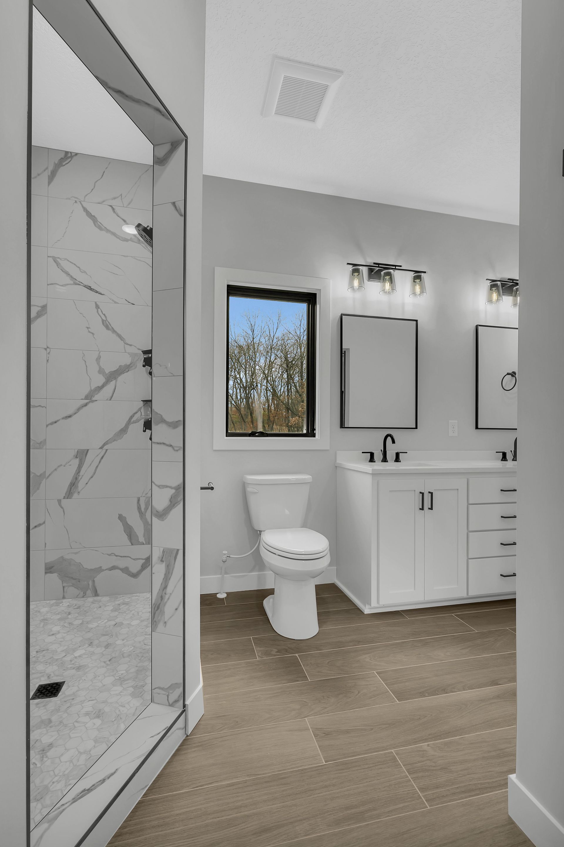 A bathroom with a toilet , sink , mirror and walk in shower.
