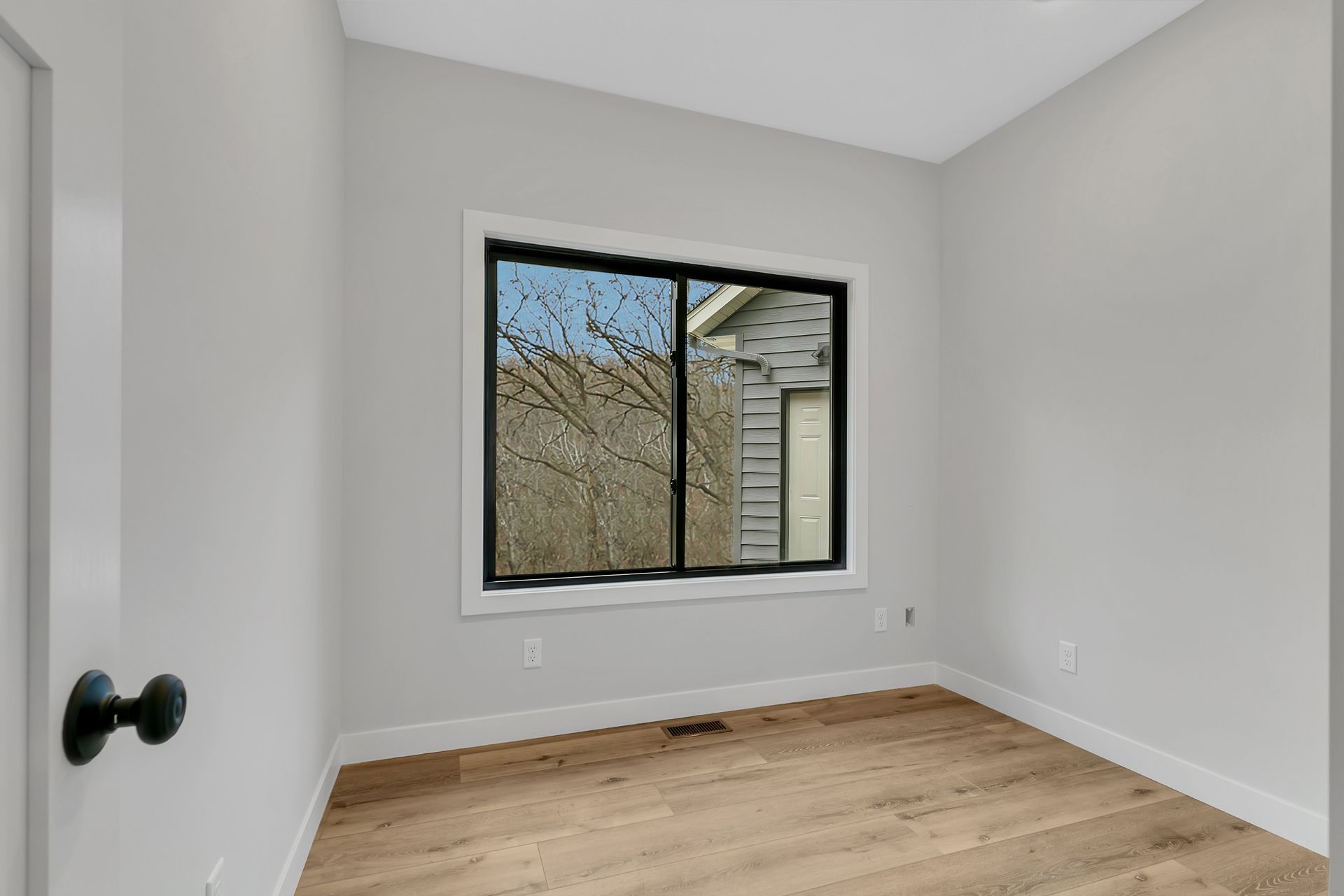 An empty room with a large window and hardwood floors.