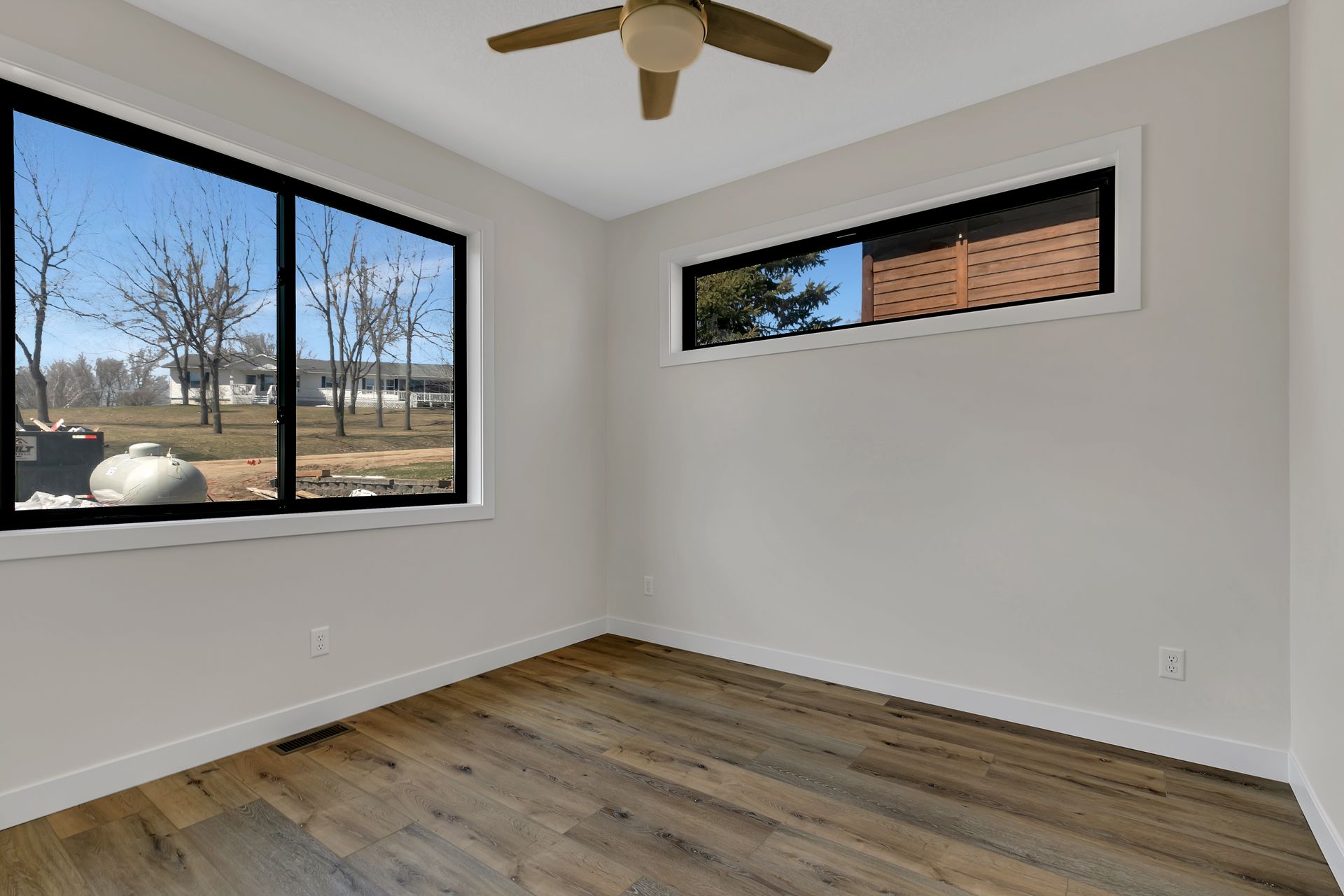 An empty room with two windows and a ceiling fan.