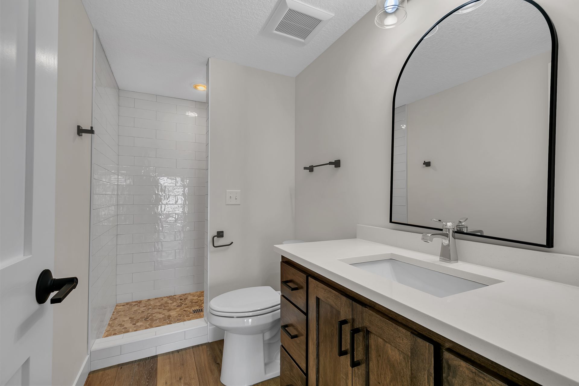 A bathroom with a toilet , sink , mirror and walk in shower.