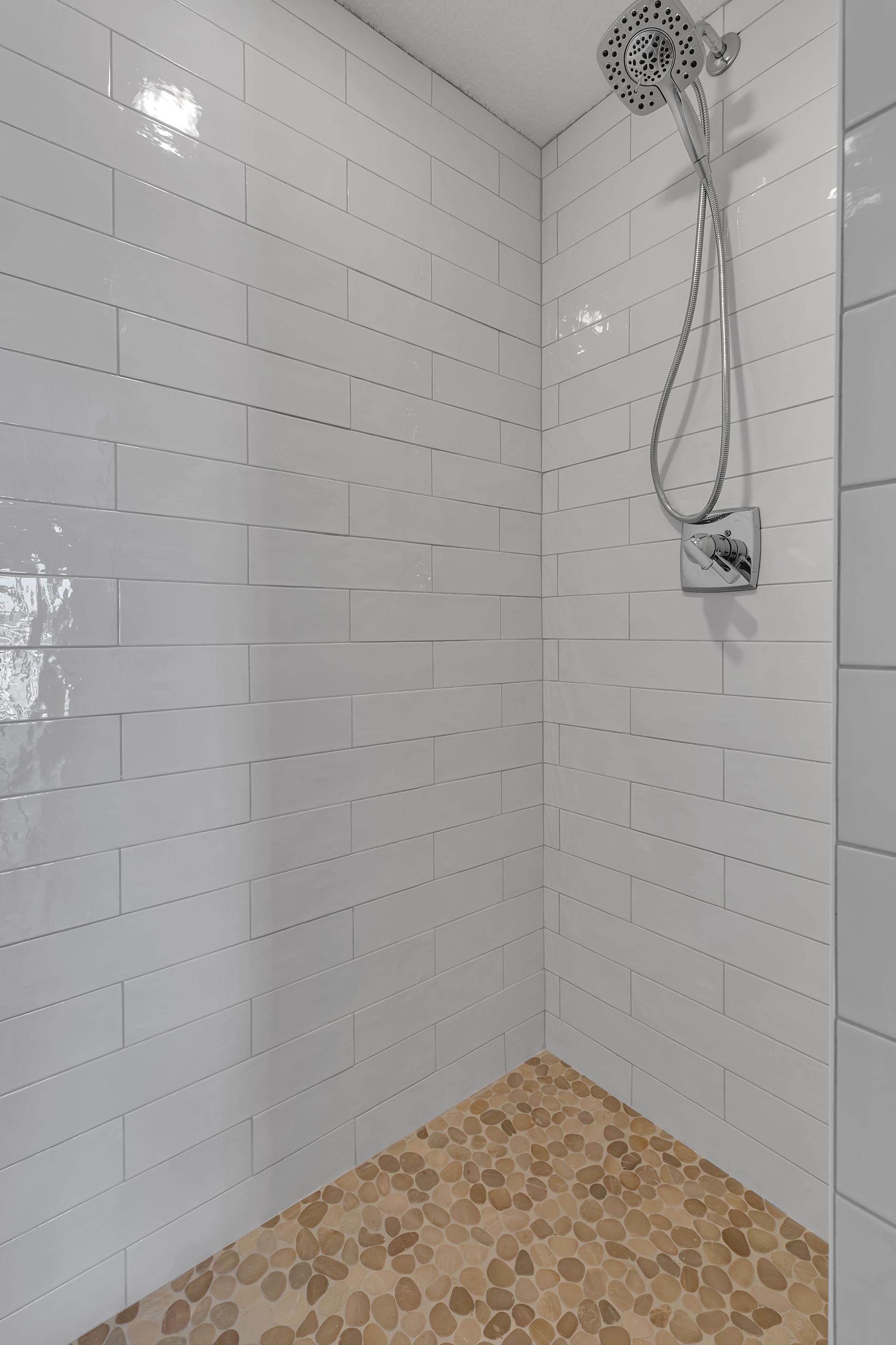 A walk in shower with white tiles and a wooden floor.
