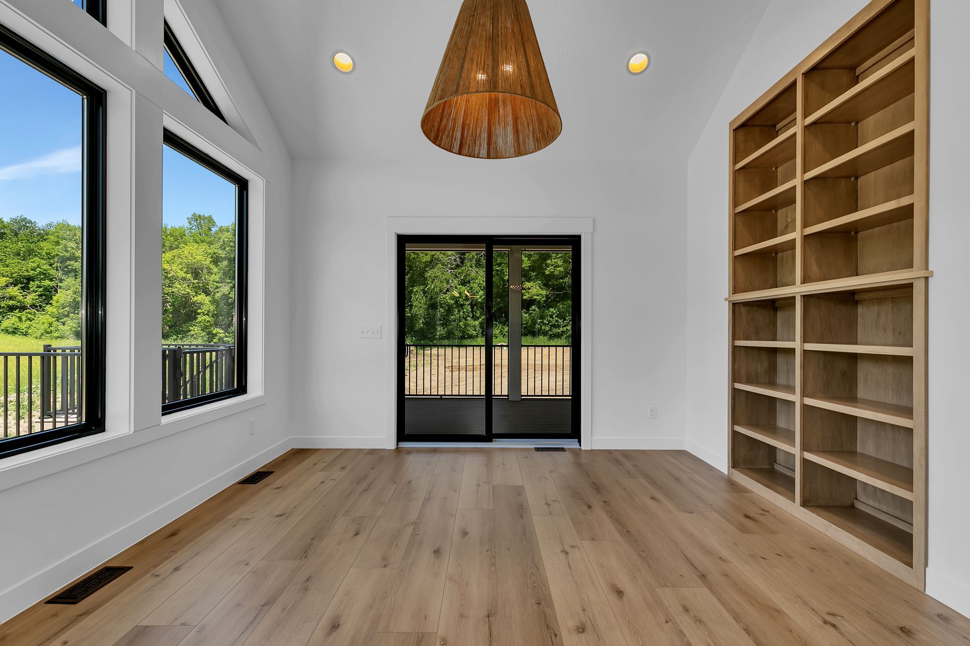 An empty room with hardwood floors , shelves and a chandelier.