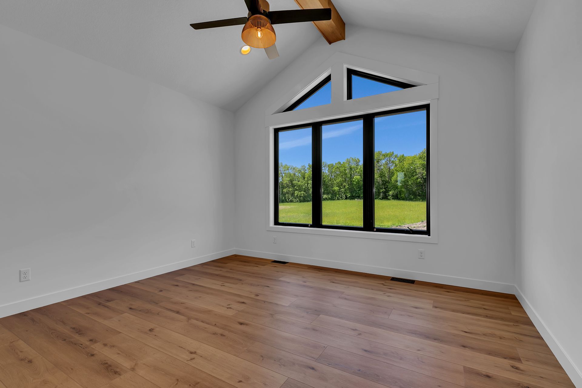 An empty room with a large window and a ceiling fan.