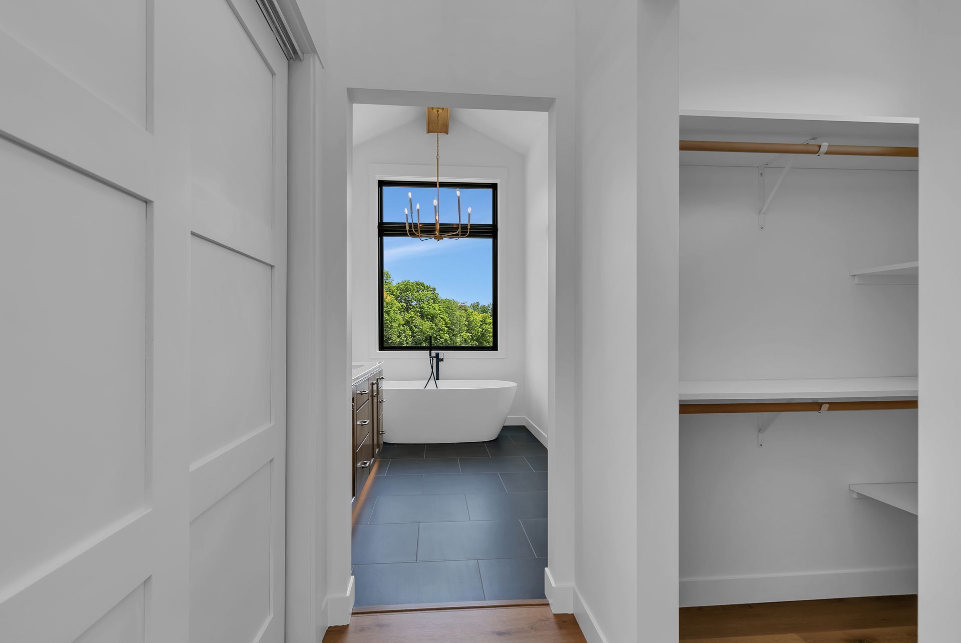 A hallway leading to a bathroom with a tub and a window.