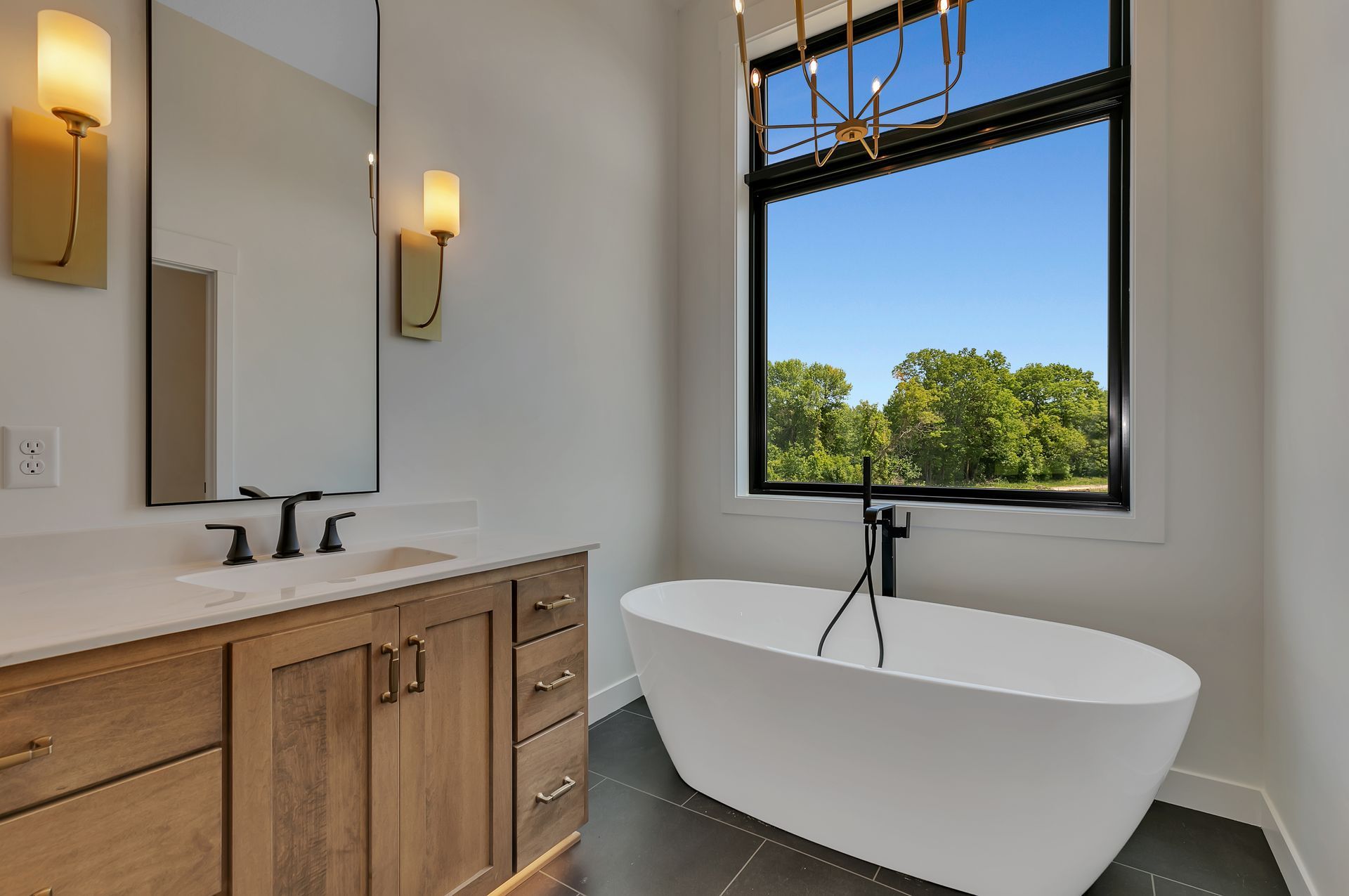 A bathroom with a tub , sink , mirror and window.