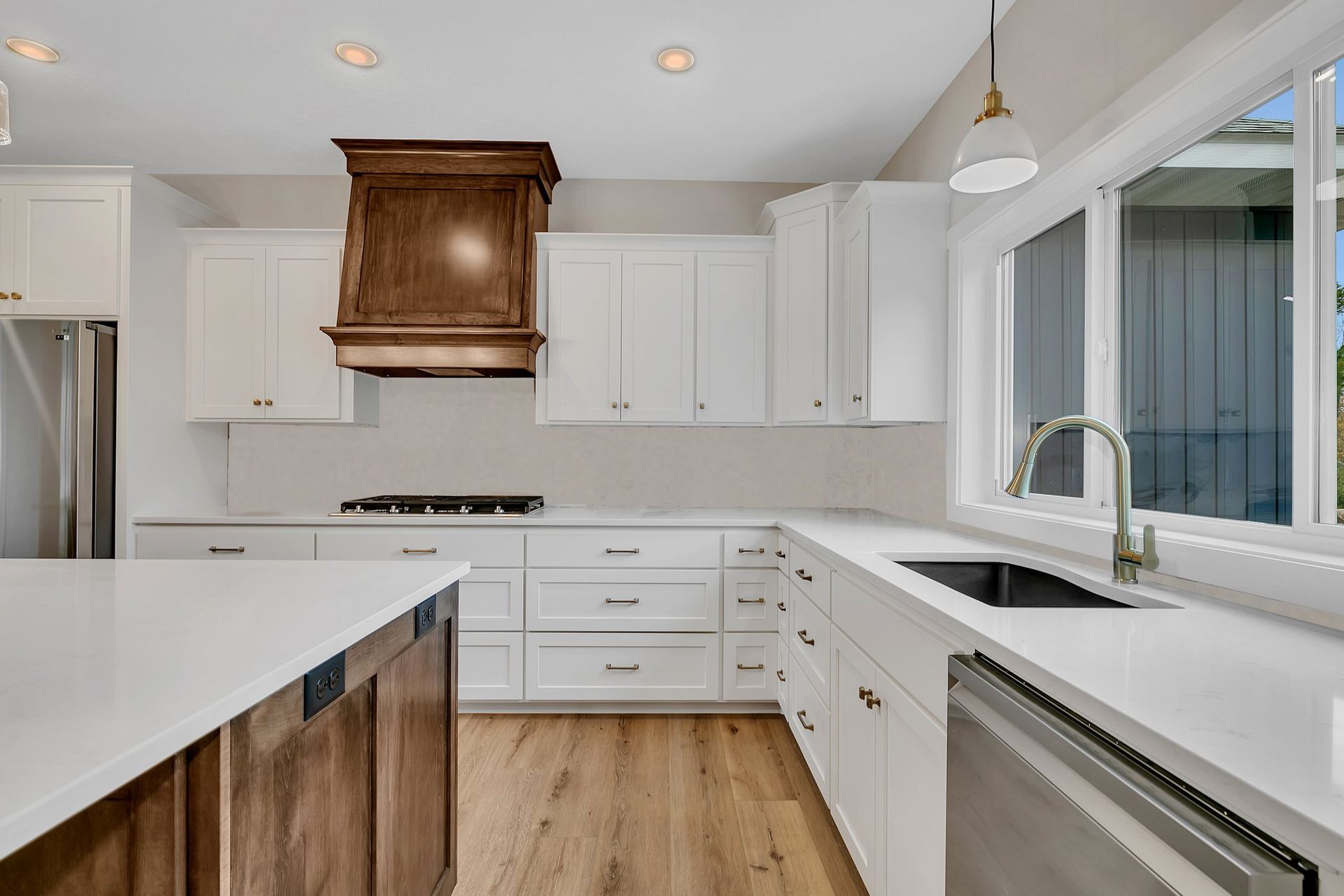 A kitchen with white cabinets , a sink , a stove , and a window.
