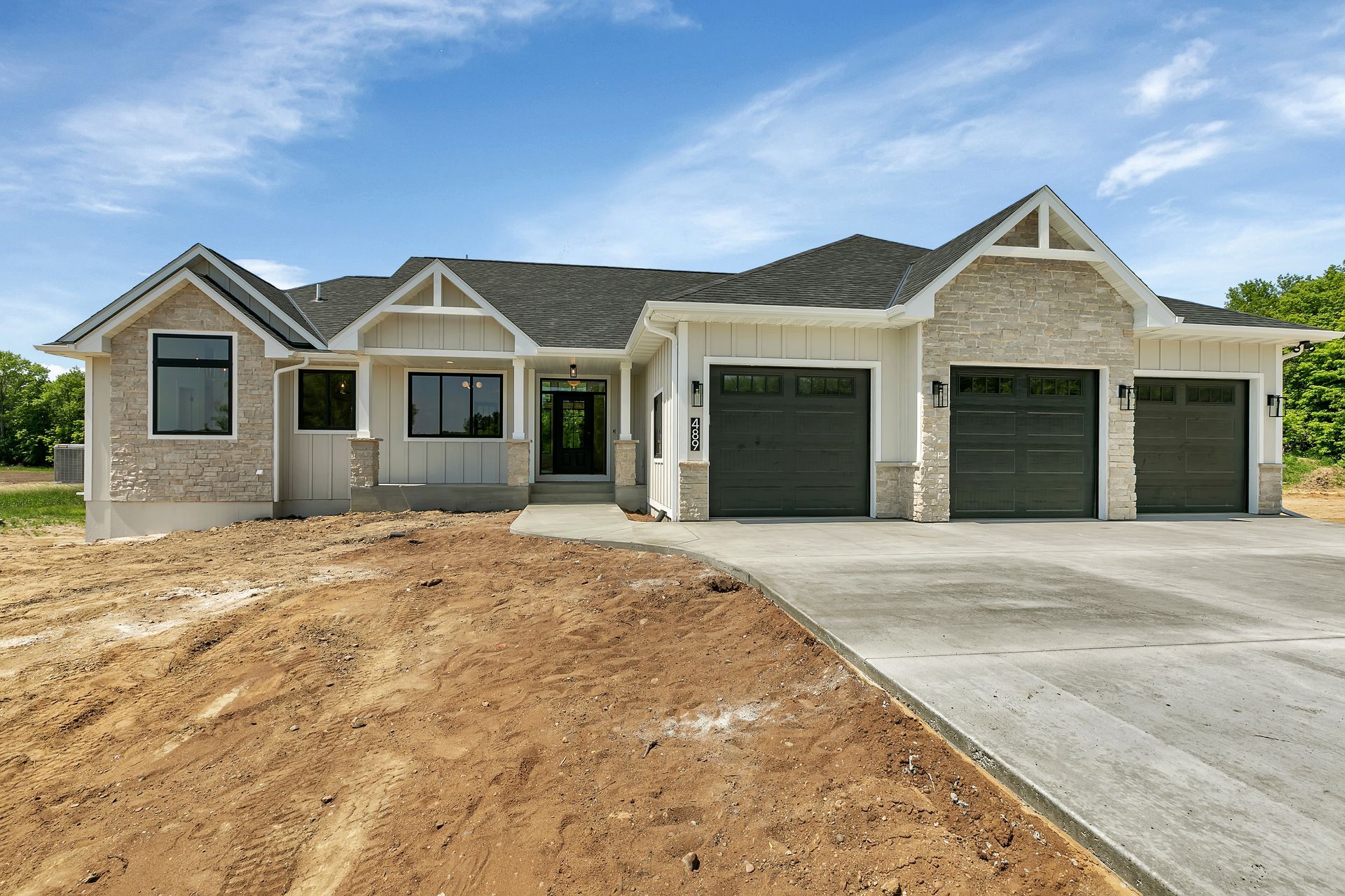 A large house with three garage doors is sitting on top of a dirt field.