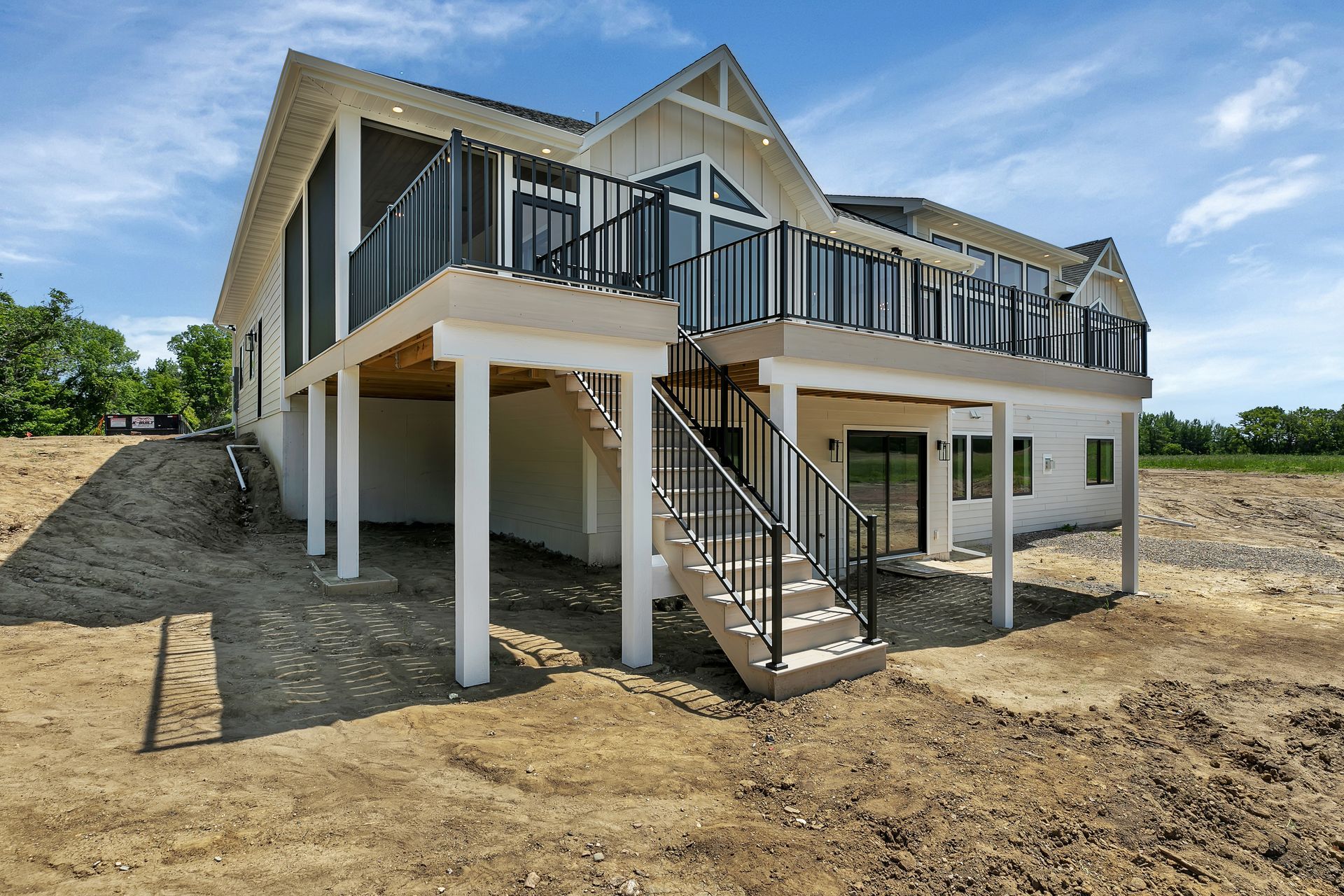 Elevated beige house under construction with black railings and exterior stairs on a dirt lot