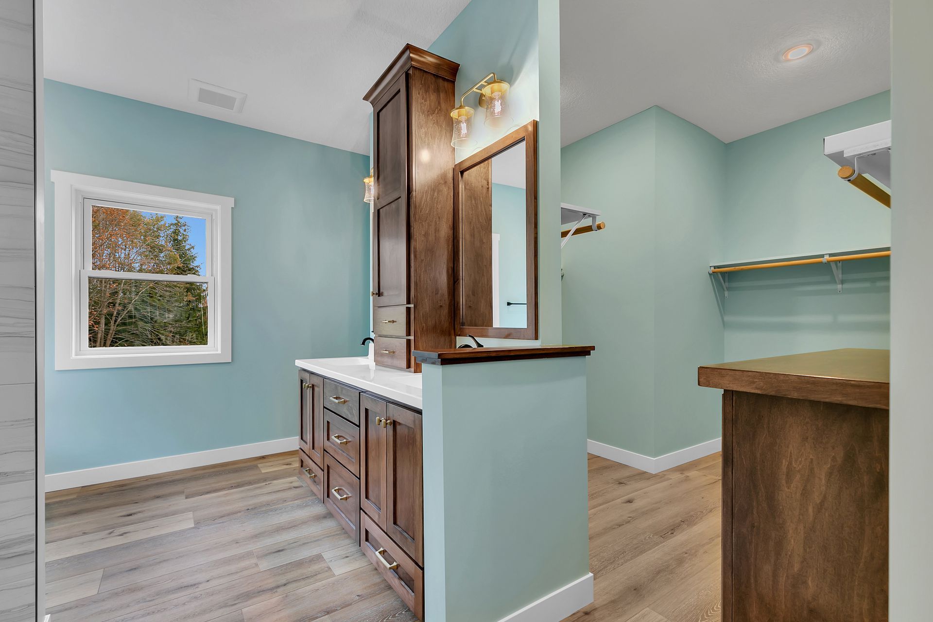 A bathroom with a sink , mirror , cabinets and hardwood floors.