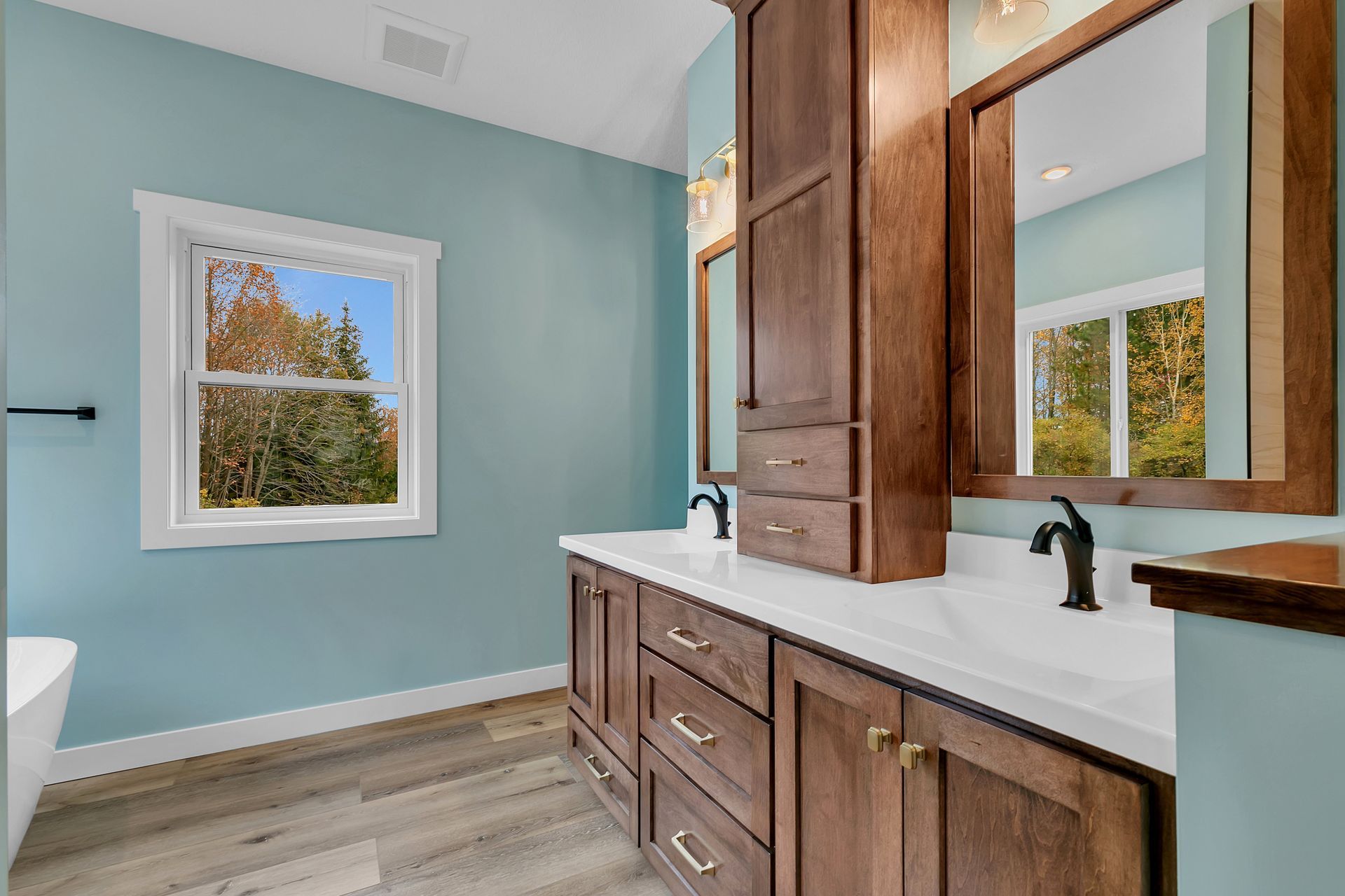 A bathroom with two sinks , two mirrors and a window.