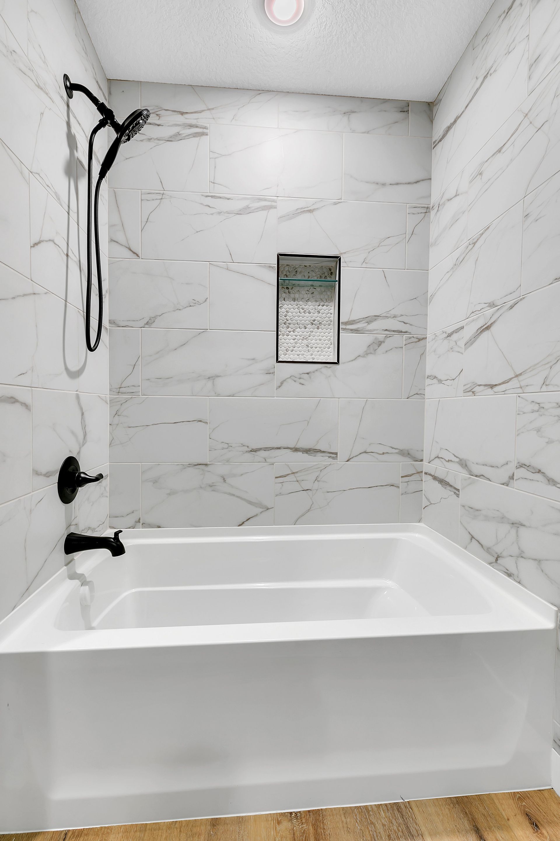 There is a bathtub in the bathroom with marble tiles.