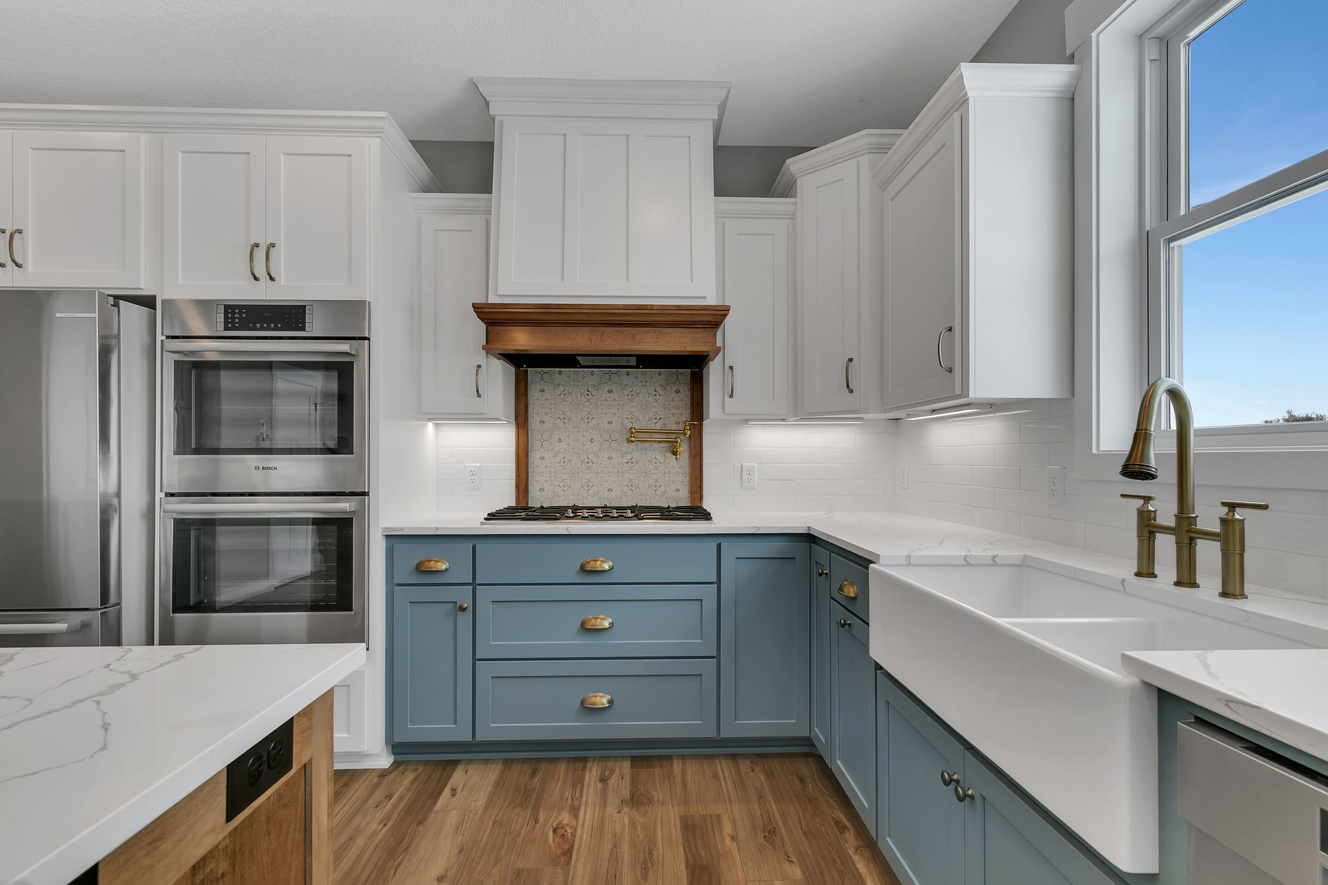 A kitchen with blue cabinets , white cabinets , stainless steel appliances , a sink , and a window.