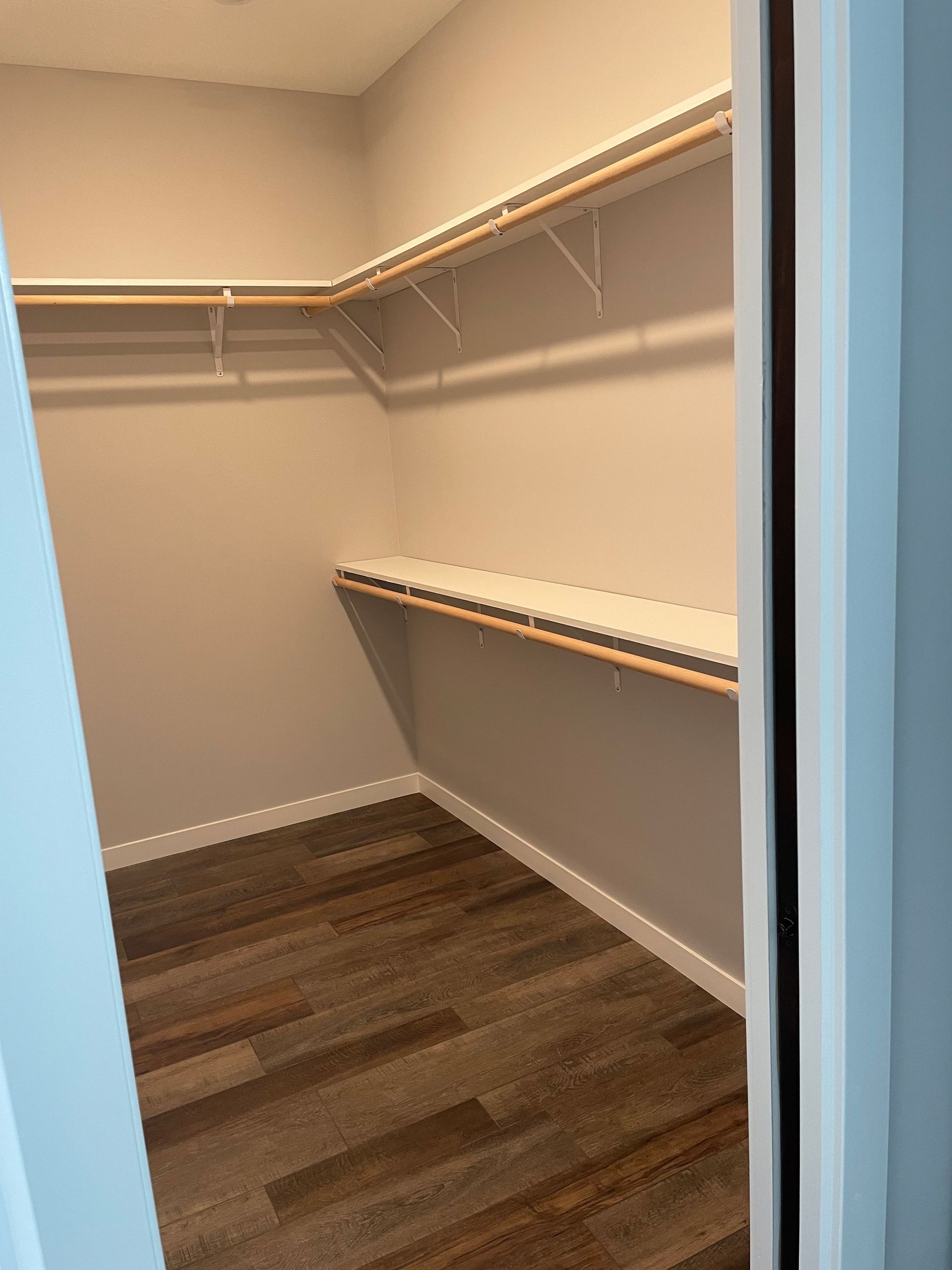 An empty walk in closet with wooden floors and shelves.