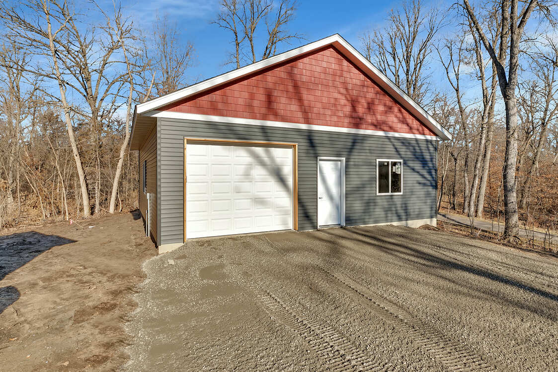 A garage with a red roof is sitting on top of a gravel road.