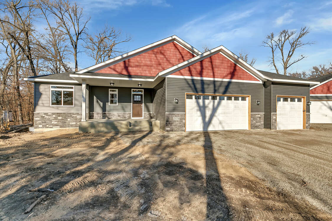 A house with a red roof and white garage doors is sitting on top of a dirt field.