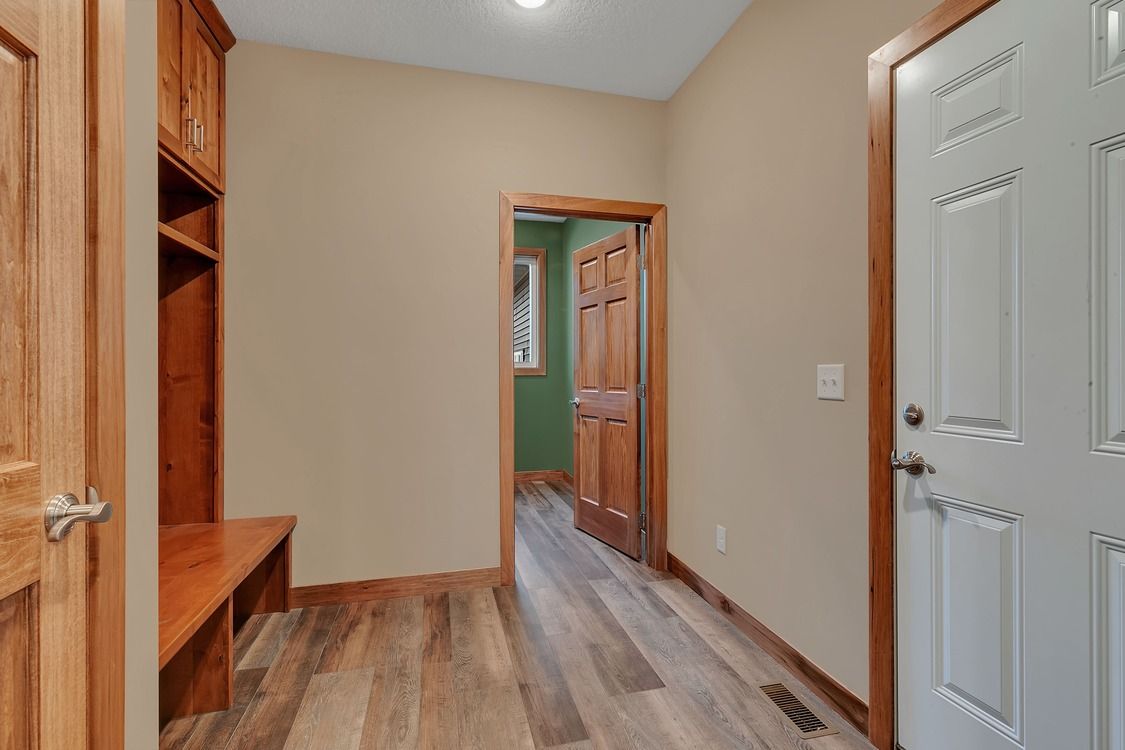 A hallway with hardwood floors and a white door leading to a room.