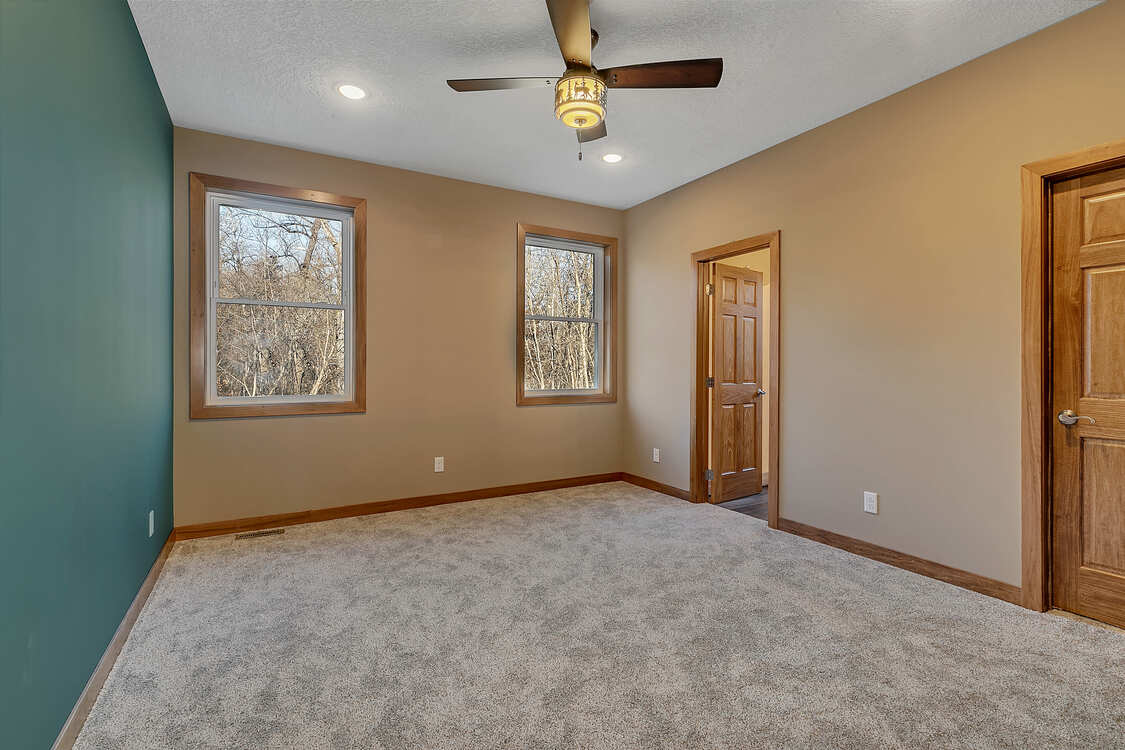 An empty bedroom with a ceiling fan and two windows.