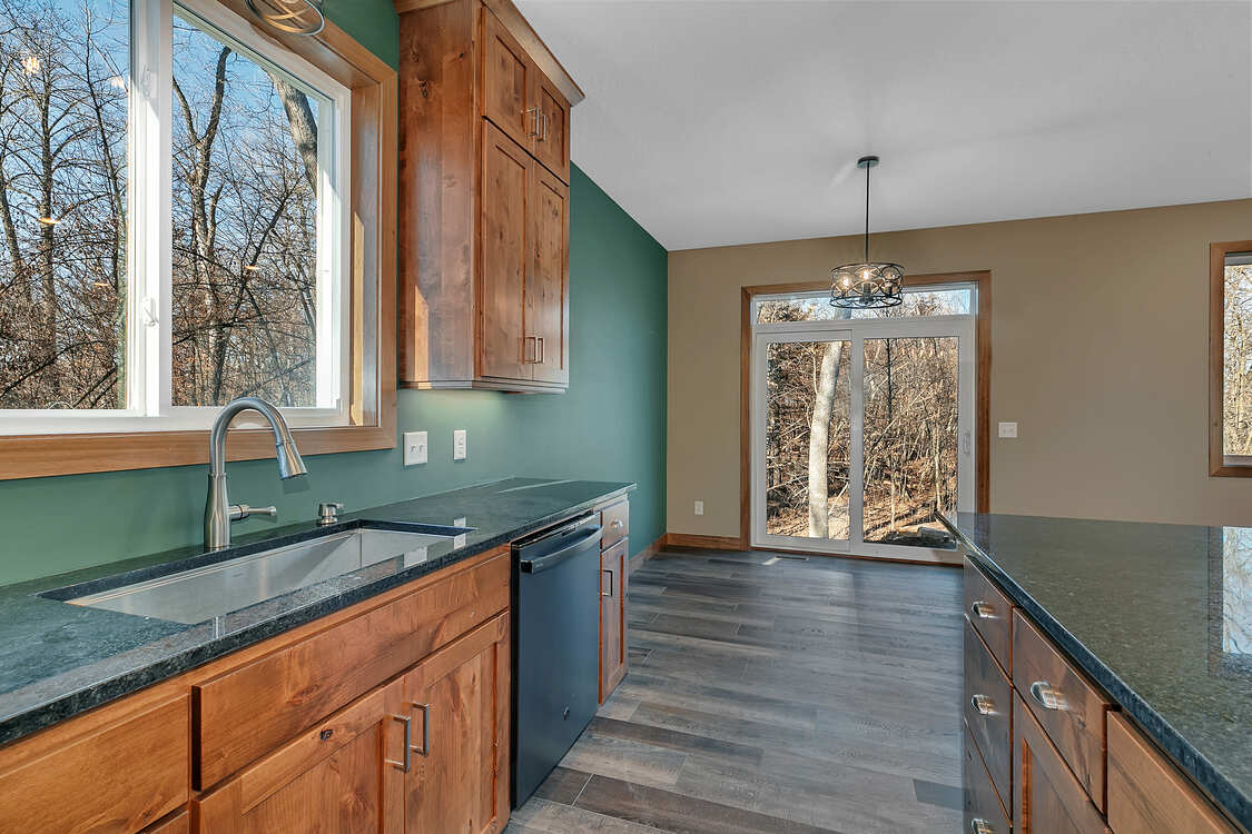 A kitchen with wooden cabinets , granite counter tops , a sink and a window.