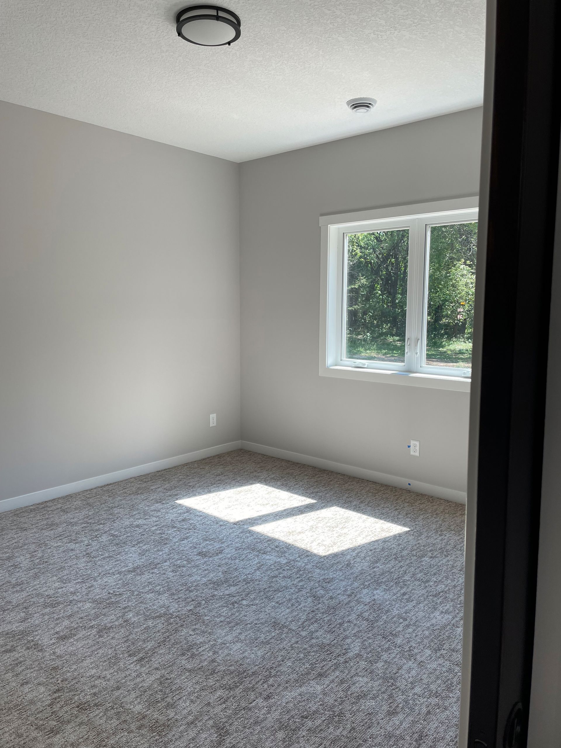An empty bedroom with a carpeted floor and a window.