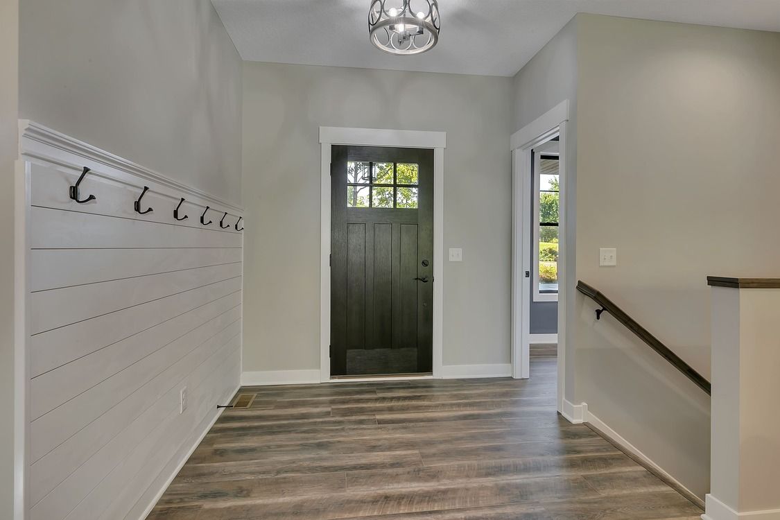 A hallway with a black door and wooden floors in a house.