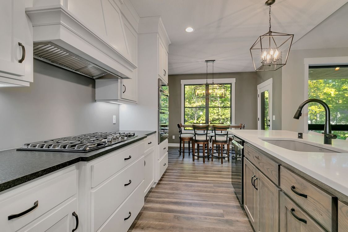 A kitchen with white cabinets and black counter tops and a stove top oven.