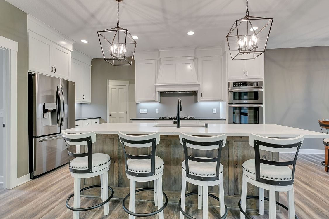 A kitchen with white cabinets , stainless steel appliances , a large island and chairs.