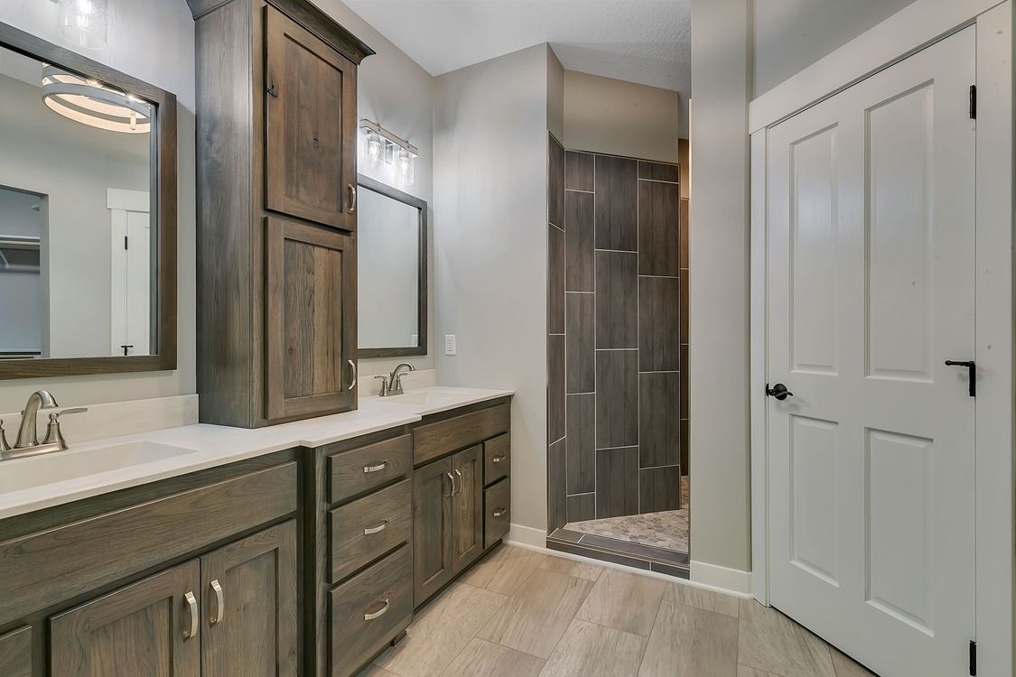 A bathroom with two sinks , two mirrors , and a walk in shower.