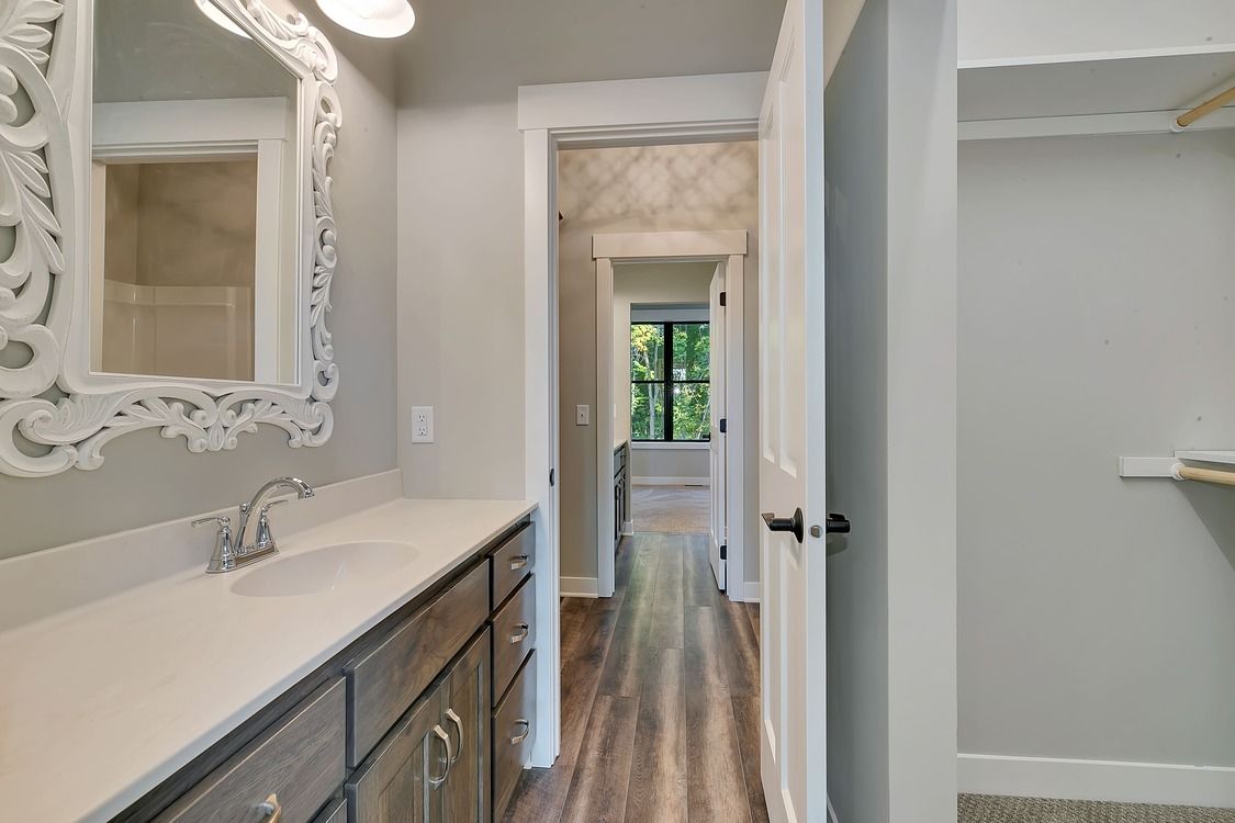A bathroom with a sink , mirror and walk in closet.