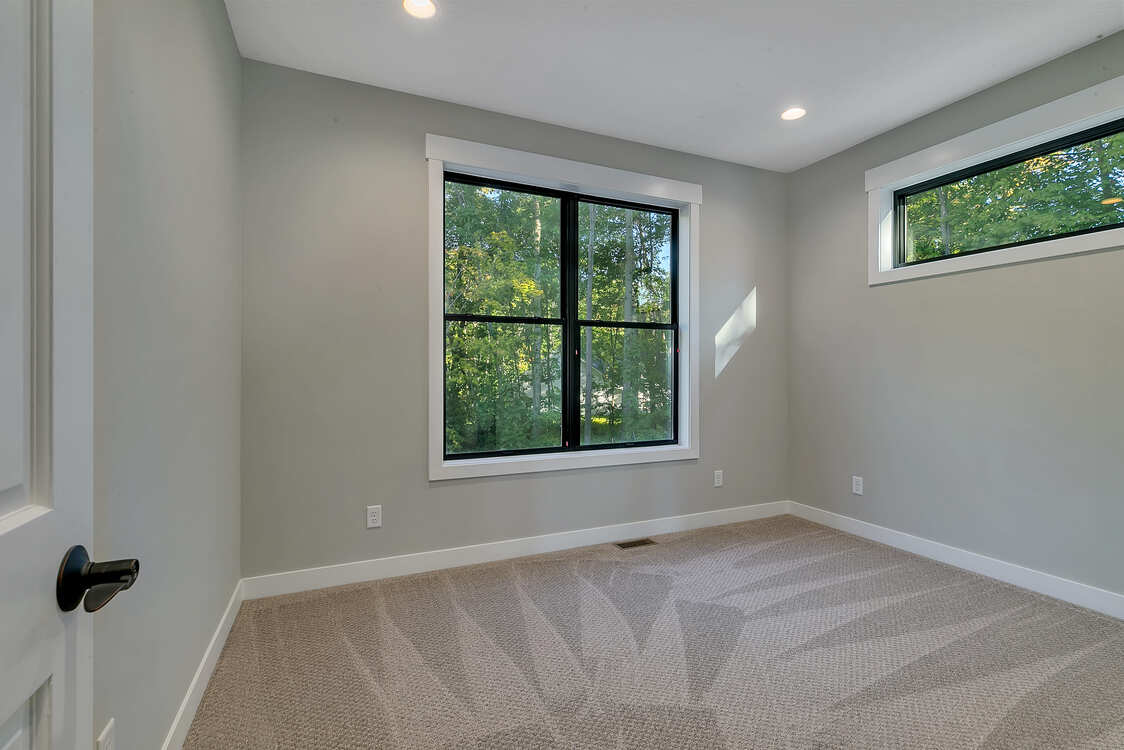 An empty bedroom with two windows and a carpeted floor.