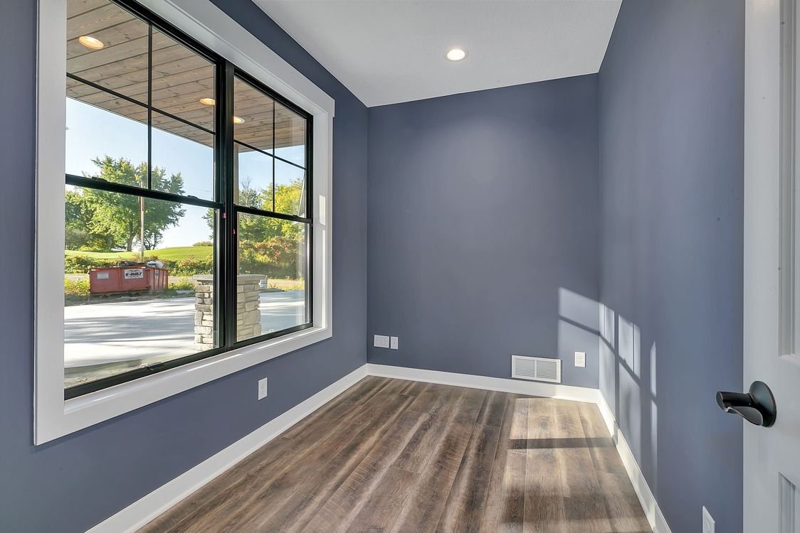 An empty room with blue walls and hardwood floors and a large window.