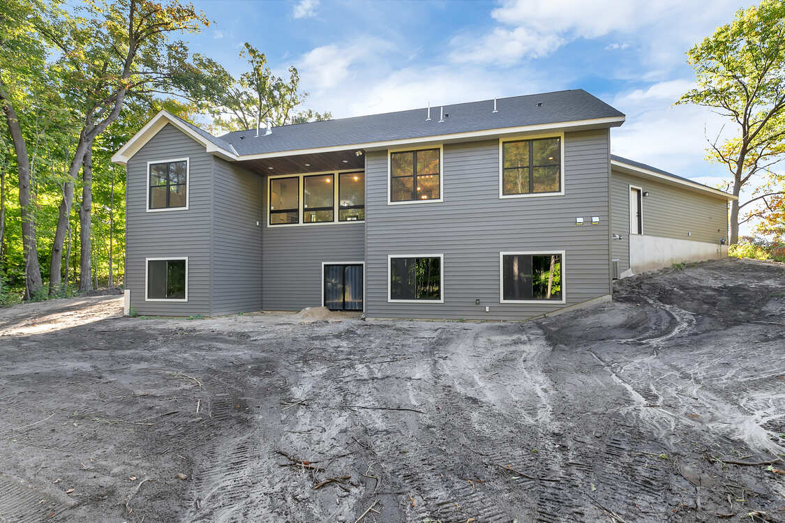 A large gray house is sitting on top of a dirt hill.
