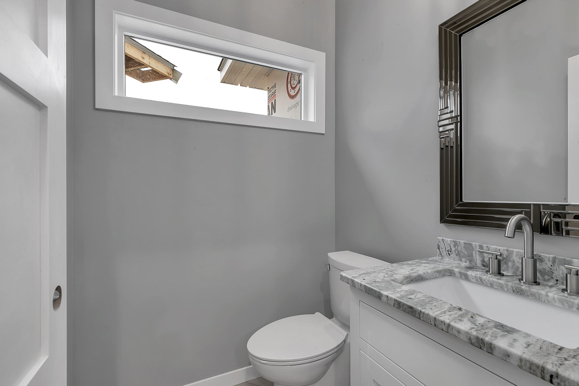 A bathroom with a toilet , sink , mirror and window.