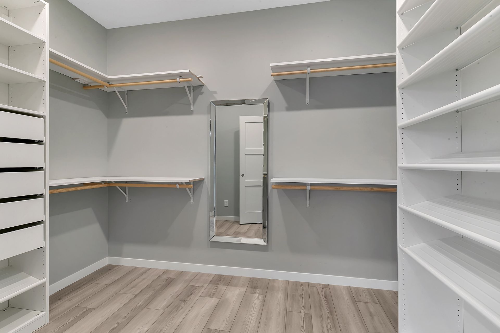 A walk in closet with lots of shelves and a mirror.