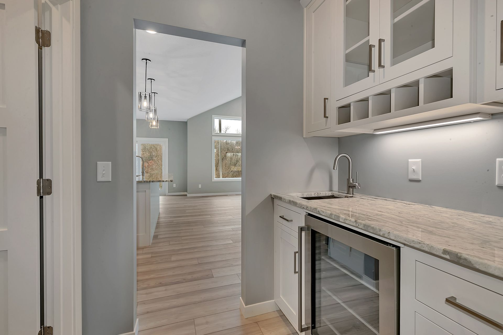 A kitchen with white cabinets , granite counter tops and a wine cooler.