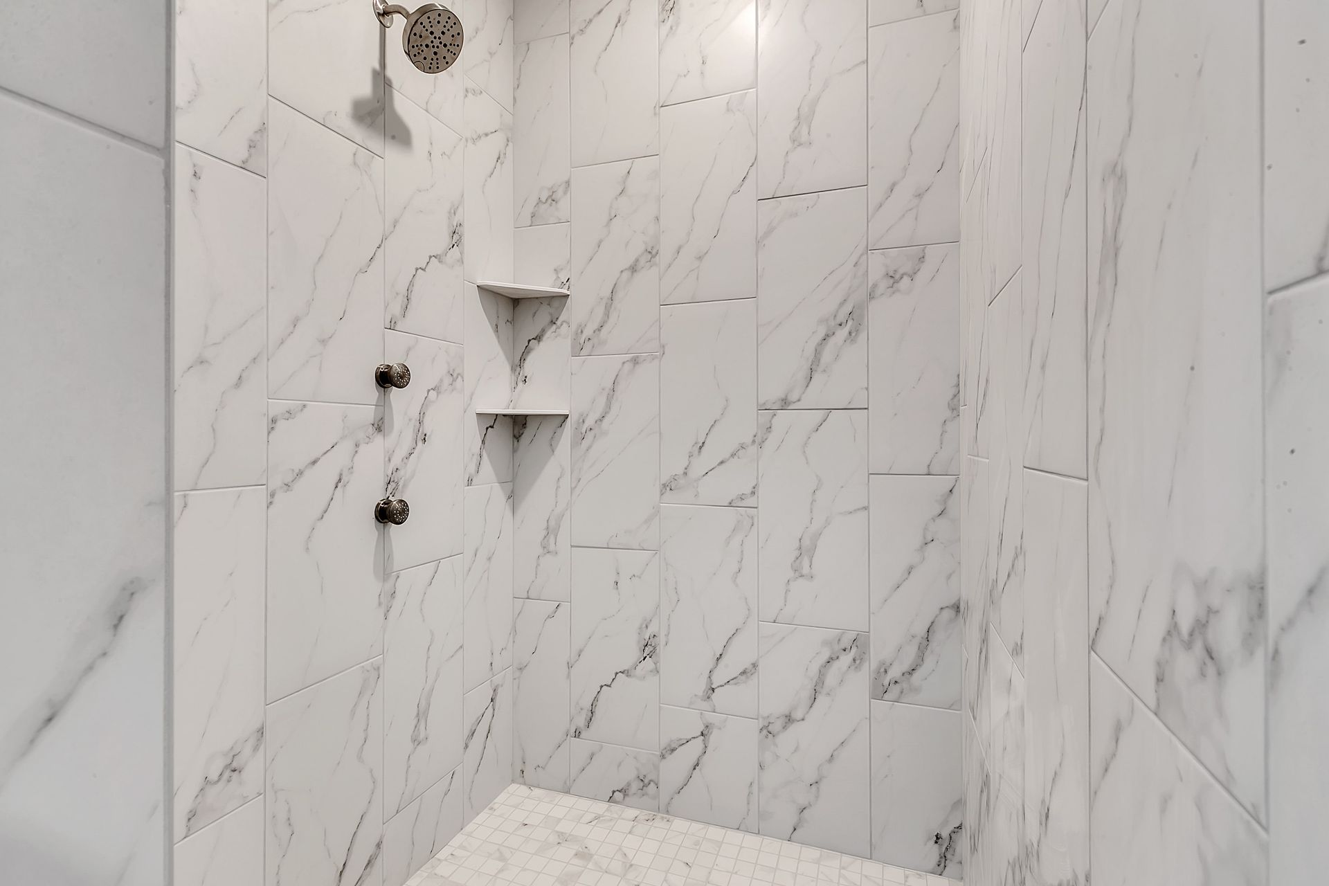 A bathroom with marble tiles and a walk in shower with a shower head.