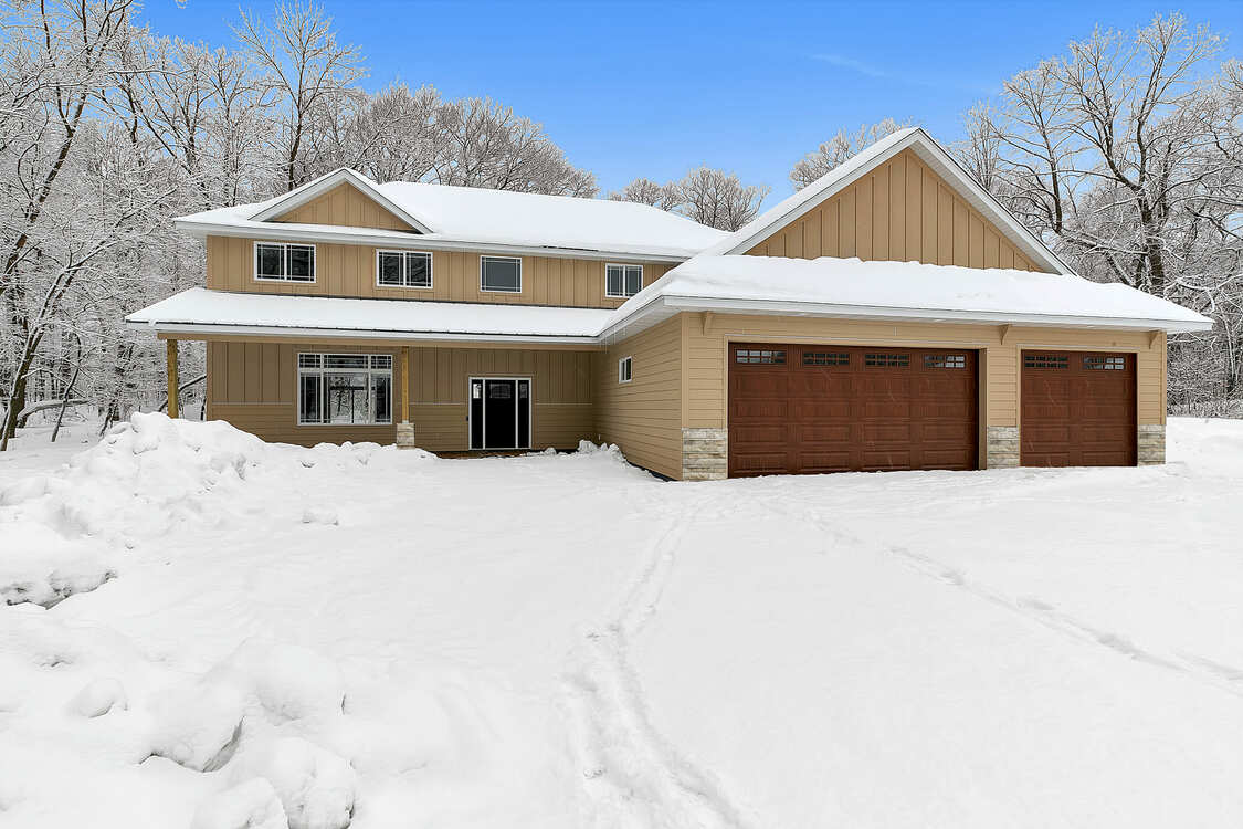 A large house with two garage doors is covered in snow.