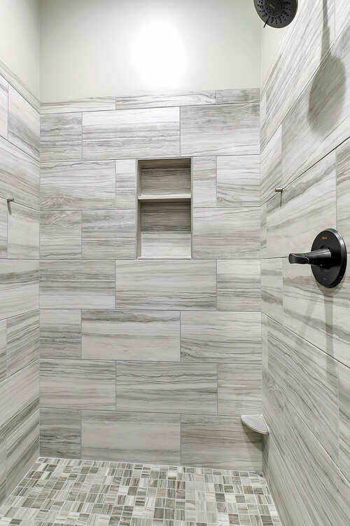 A walk in shower with tiled walls and a mosaic floor.