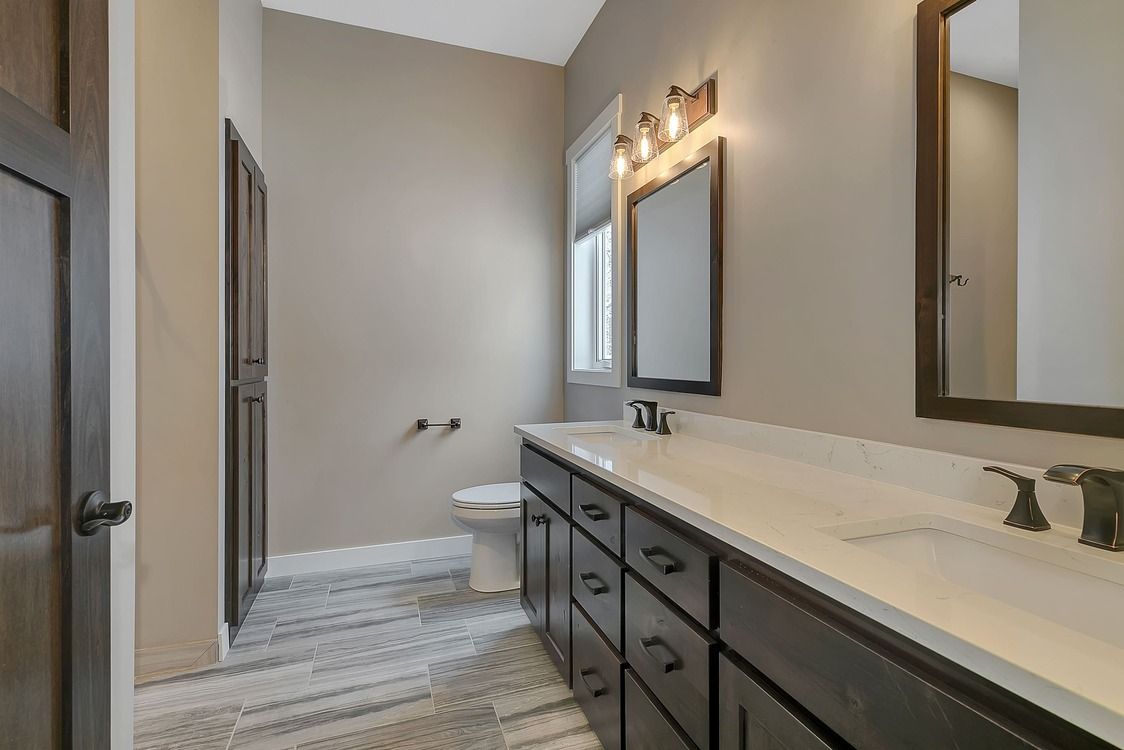 A bathroom with two sinks , a toilet , and two mirrors.