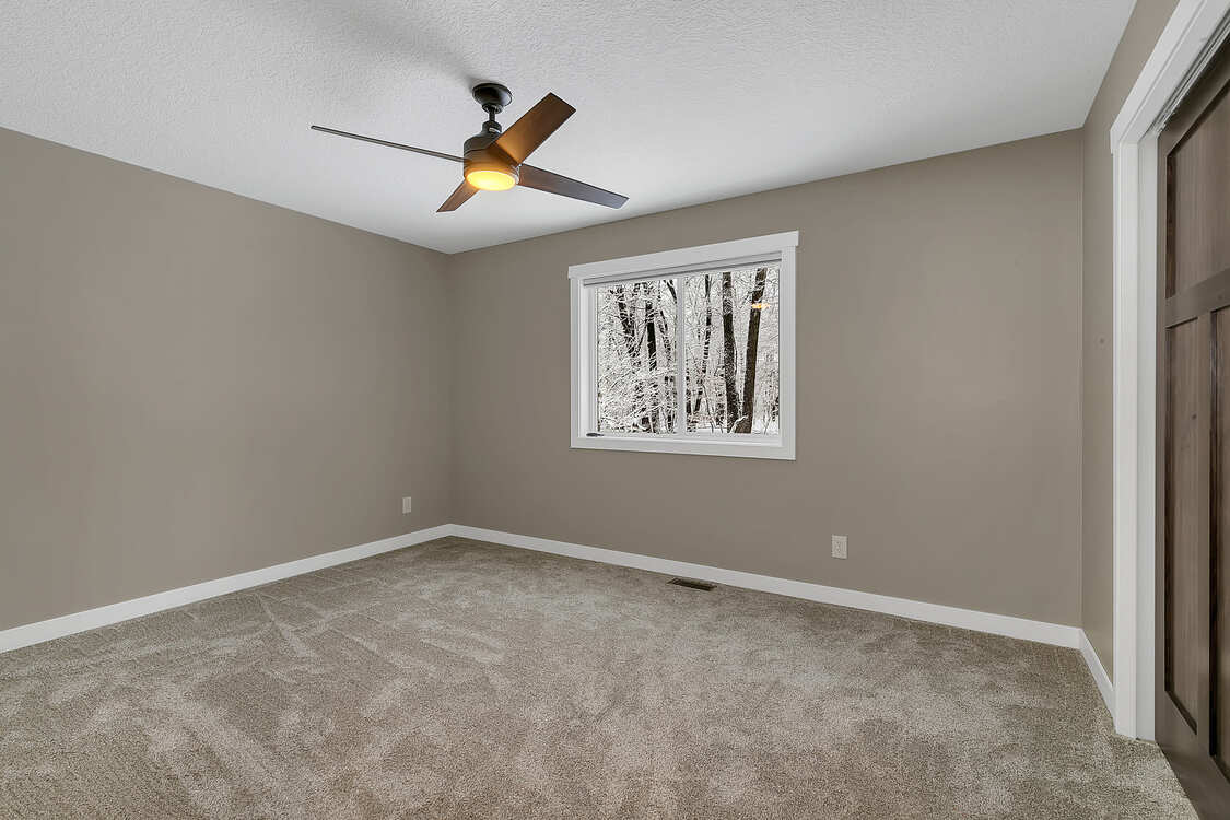 An empty bedroom with a ceiling fan and a window.