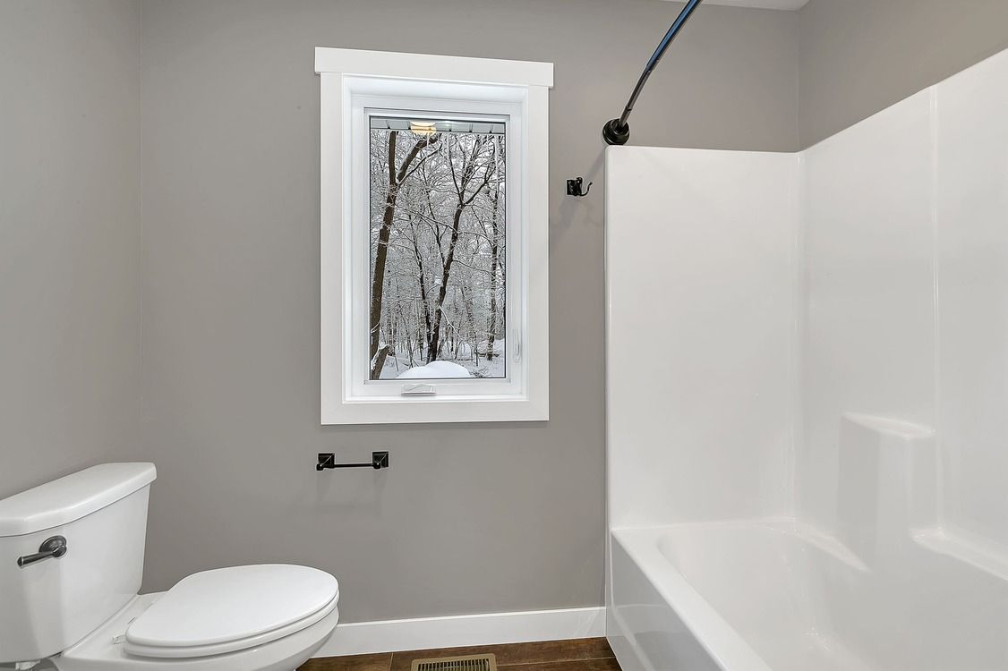 A bathroom with a toilet , tub , shower and window.
