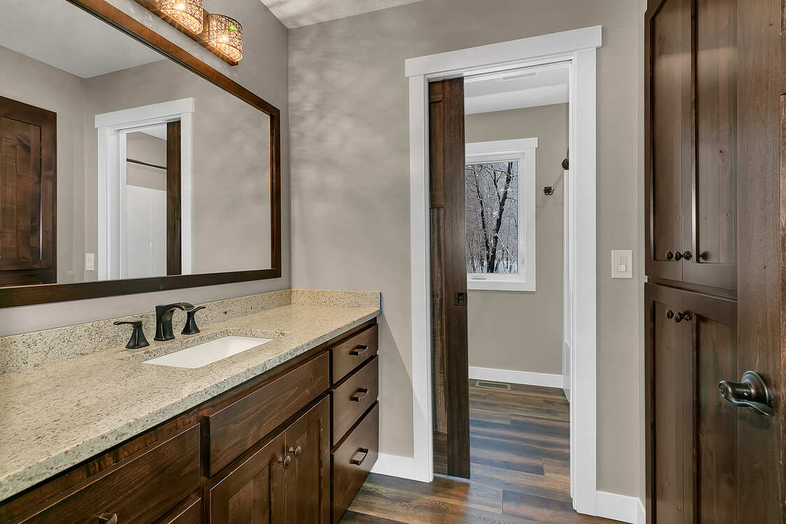 A bathroom with a sink , mirror , cabinets and hardwood floors.